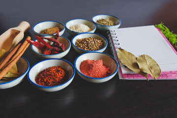 Different spices and herbs in small bowl with notebook for cooking Thai food on background.