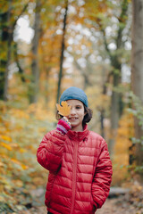 Girl with autumn leaves near her face on a walk in the forest