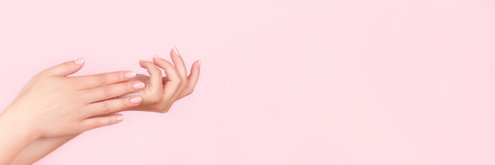 Female hands with beautiful manicure - pink nude nails on pink background, wide panoramic banner...