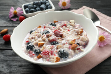 Tasty oatmeal porridge with toppings on black wooden table, closeup