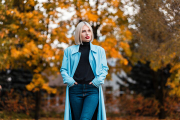 Pretty blonde business woman in fashion blazer, sweater and jeans walks in orange autumn park