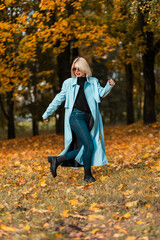 Fashion beauty girl in stylish autumn clothes look with blue coat walks on park with golden fall leaves.