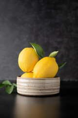 Fresh lemons fruit on dark, black background in a bowl