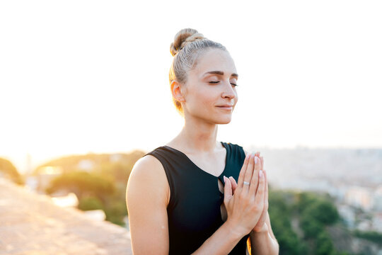 Peaceful woman with namaste gesture meditating on rooftop