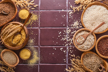 White, brown and red rice, buckwheat, millet, corn groats, quinoa and bulgur in wooden bowls on a brown stone kitchen table. Gluten-free cereals. Top view with copyspace