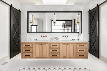 Bathroom in luxury home with double vanity. Features floating hardwood cabinets and faucets, large mirror, and elegant tile floor.  A skylight allows for abundant natural light.
