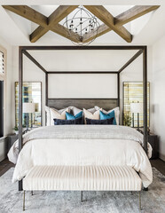 Bedroom detail in new luxury home. Features bedding and lamps, pillows, wood beams above bed with skylight and pendant light, abundant natural light.