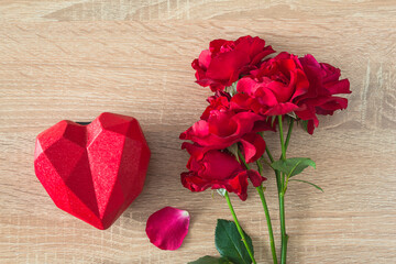 Valentine's day greeting card; Bouquet of red roses and gift box shape heart on wooden background top view