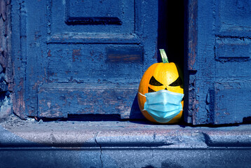 Halloween background. A naughty pumpkin wearing in a medical mask peeking out from behind an old...