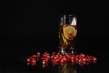 Drink in a glass with mint, pomegranate and lemon on a black background