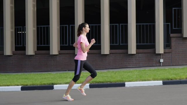 Woman in sportswear jogging against modern building in slow motion. Tracking shot fit female doing training in the morning. Concept of fitness