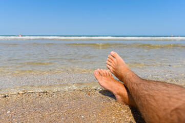 Male legs on the beach next to the sea. Ideal seaside resort concept. Selective focus on legs.