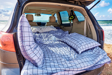 Pillows and a duvet in a car trunk by the ocean.
