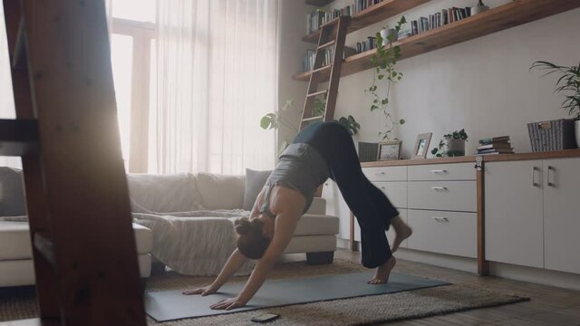 healthy yoga woman exercising at home practicing three legged downward facing dog pose in living room enjoying morning fitness workout