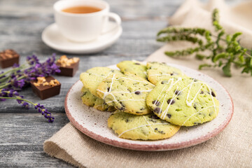 Green cookies with chocolate and mint with cup of green tea on gray wooden background. side view, close up, selective focus.