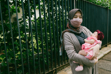 Happy asian mom holding her little baby daughter wearing hijab and Mask