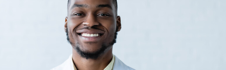 Obraz premium young and happy african american doctor smiling at camera on white background, banner