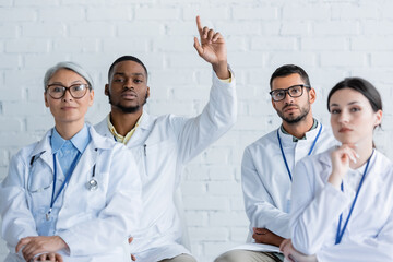 young african american doctor raising hand near multiethnic colleagues during medical seminar