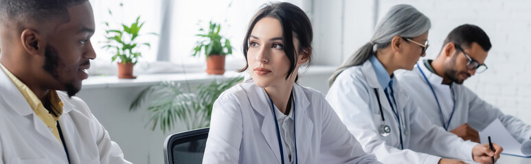 interracial physicians talking during medical council near blurred colleagues, banner