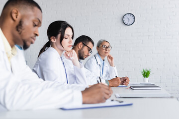 Fototapeta premium blurred african american doctor writing near colleagues during council in hospital