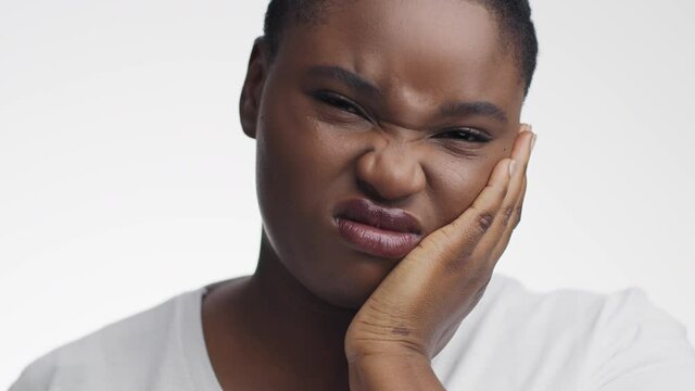 Upset young african american woman touching her cheek and looking sadly at camera, suffering from tooth pain