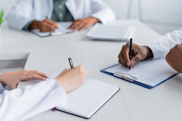 Fototapeta premium cropped view of multiethnic doctors writing during council in meeting room