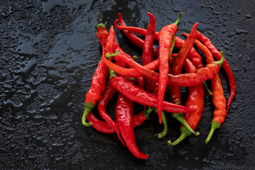 Hot chili heap on wet black slate. Pile of de cayenne long slim peppers in water.