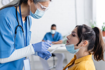 mature asian doctor in medical mask taking samples for pcr test from young woman in hospital