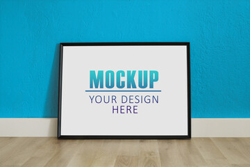 Frame, poster mock up with horizontal black frame. Empty frame standing on the wooden floor, blue wall. Free space for your picture or text, copy space. Minimalist design.
