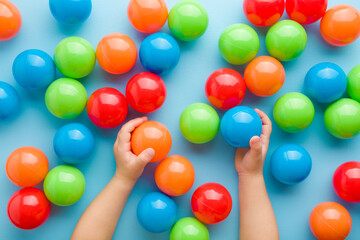 Baby hands playing with colorful plastic balls on light blue floor background. Pastel color....