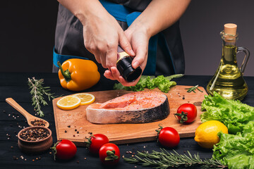 Hands chop the spices on the salmon steak. The recipe for cooking fish. Lemon, rosemary, spices, tomatoes, cutting board. Close-up. Side view.