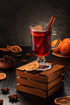 One glass of mulled wine with cinnamon sticks and orange slices and anise stars on a wooden stand on a dark background. Recipe, preparation of mulled wine. Vertical photo.