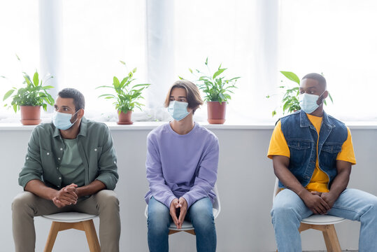 Young Multiethnic Men In Medical Masks Sitting In Line While Waiting For Vaccination