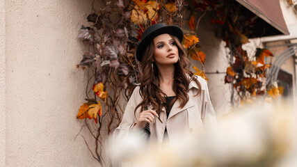 Fashionable portrait of a beautiful glamorous girl model with a hat in a classic gray coat with a handbag walks in a city with yellow autumn foliage