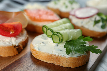 Fototapeta na wymiar Toasted bread with cream cheese, cucumber and parsley on wooden board, closeup