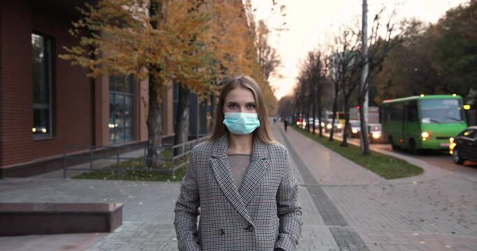 Waist up portrait view of the caucasian girl wearing protective mask looking at the camera while walking in the street during pandemic. Outdoor portrait of the happy female tourist