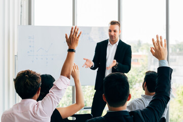 Many business people participants raising up their hand in business seminar conference event inside corporate company office with speaker in front