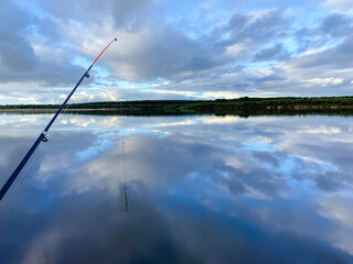 A landscape with a fishing rod, a spinner, river expanses and beautiful skies. Fishing concept.