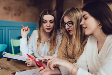 Girlfriends using smartphone while sitting in cafeteria and having pleasant conversation