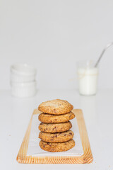 Homemade cookies on wooden cutting board and a glass of milk on white background.