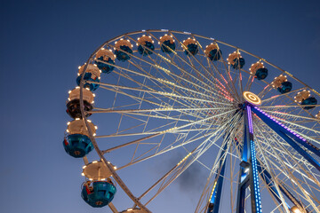 Low angle view of colourful illuminating Ferris wheel at carnival amusement park, against beautiful...