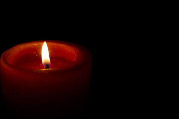Candle flame in the dark. Burning red candle on a black background.
