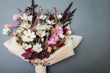 Fresh bouquet of white pink flowers with burgundy foliage wrapped in paper and arranged on grey background.