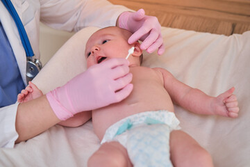 The doctor performs the hygiene of the nose and ears of the newborn baby with a cotton swab. Nurse...