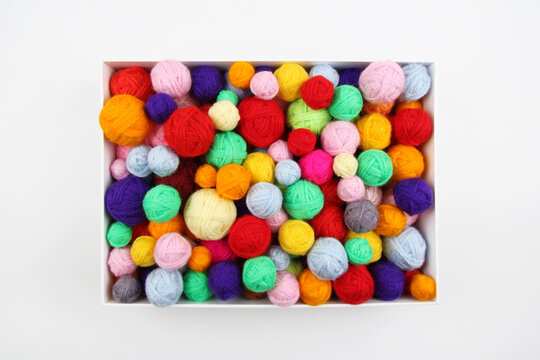 A lot of multi-colored wool balls of knitted yarn in a cardboard box on a white background.The concept of handmade work, needlework and the sale of thread,a favorite hobby.Top view.Copyspace.