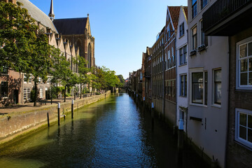 View on typical dutch water canal with gothic church facade and residential houses against blue summer sky - Dordrecht, Netherlands