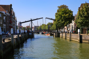 Dordrecht, Netherlands - July 9. 2021: View over water canal on typical dutch drawbridge, boats and old houses against blue summer sky