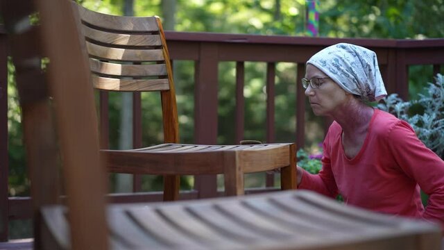 Slow motion of mature woman applying varnish to teak table furniture in garden area at home.