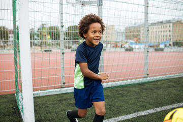 Little boy playing football. African American schoolboy at stadium. Young kids running outside....