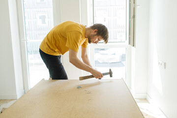 Man assembling furniture at home. Self service kitchen cabinets. Moving in new apartment. Adult making DIY workshop. Young male repairing home. Installing shelves in new home insurance. hammer in hand